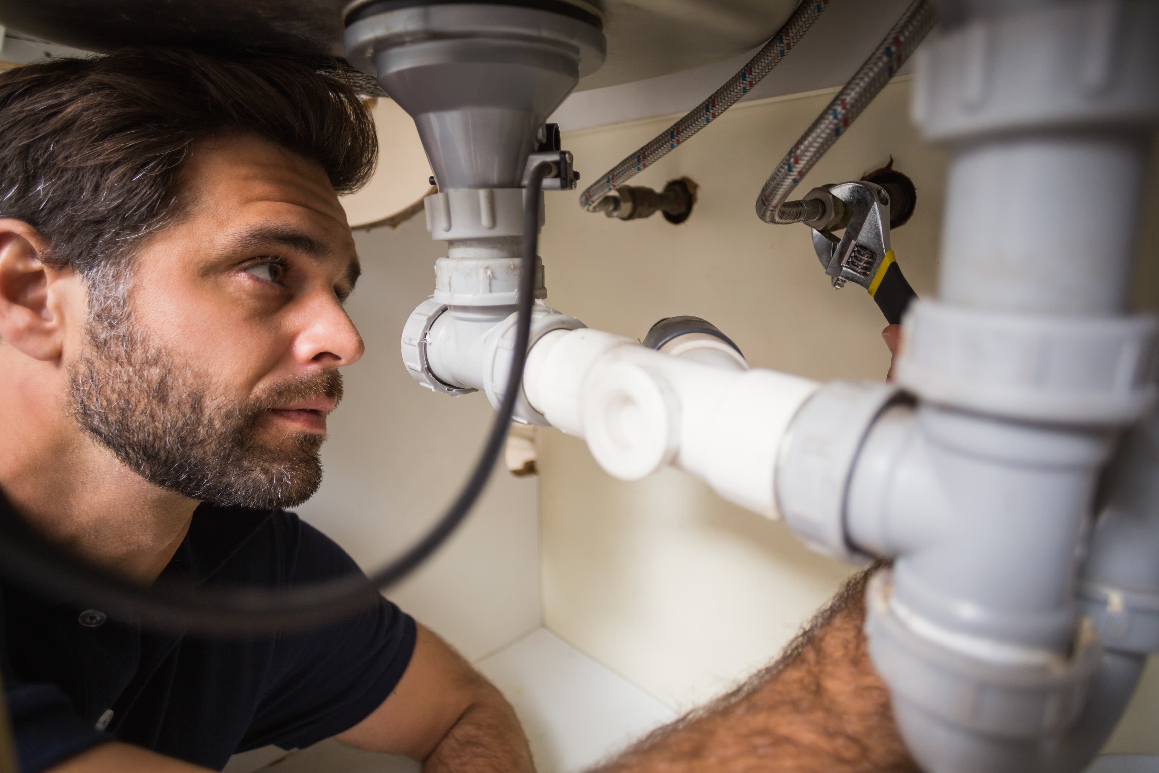 Plumber inspecting waste pipes under a sink